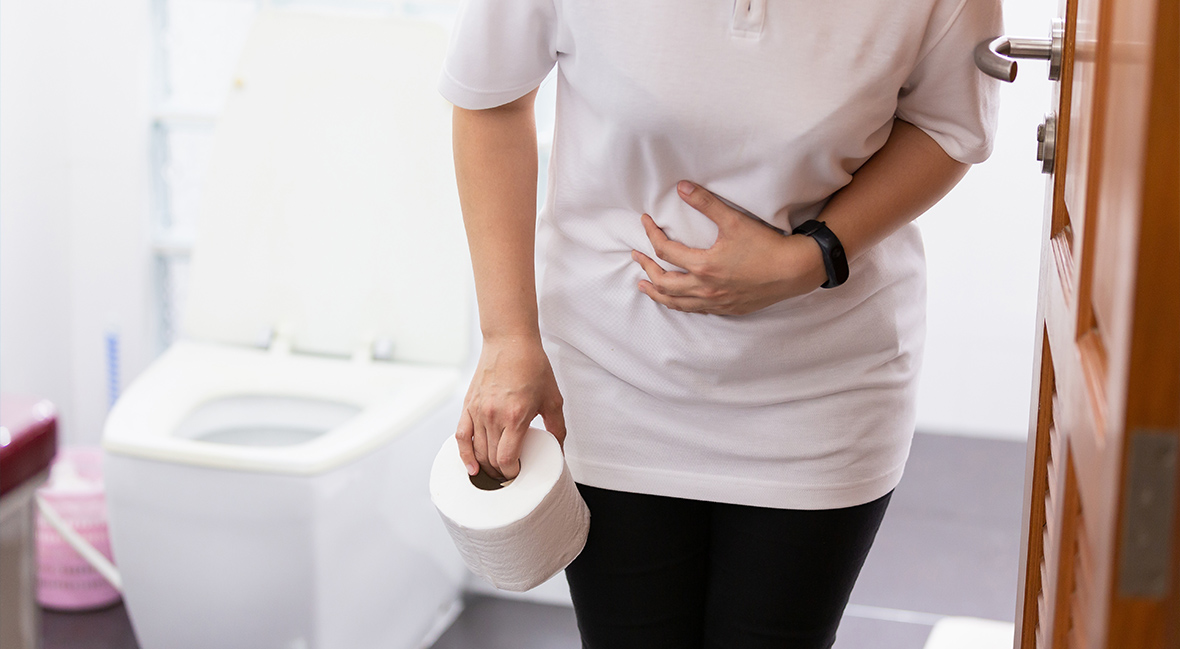 woman exiting the bathroom holding a roll of toilet paper and clutching her stomach